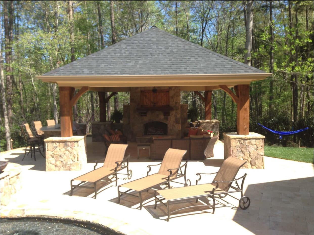 Cedar pavilion with hipped roof and stone fireplace by Vivid Outdoor Living